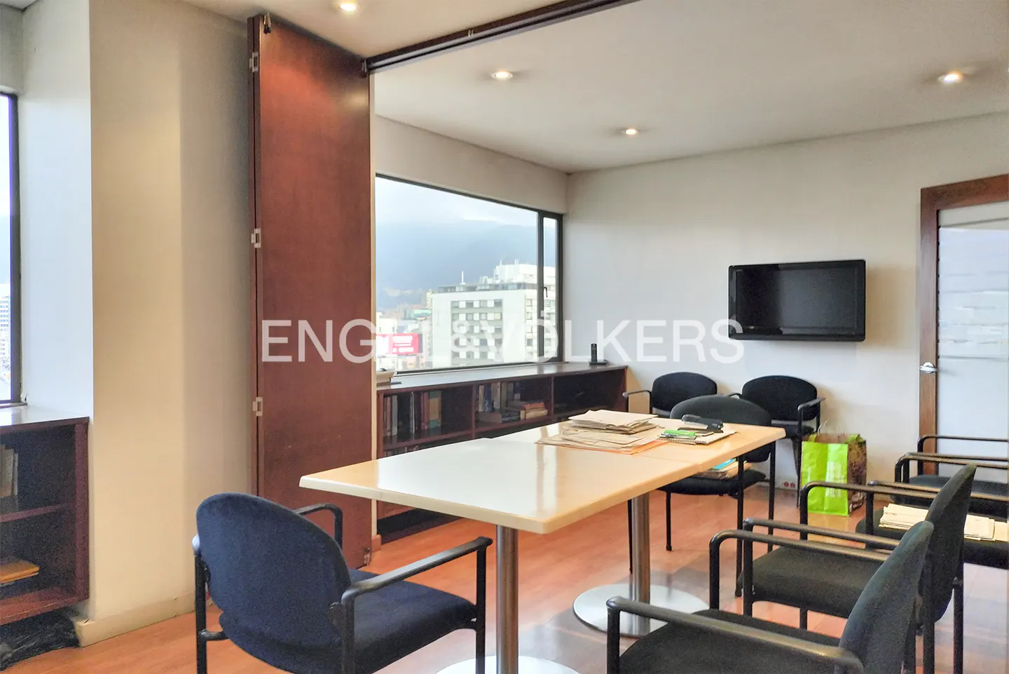 Office space with a large window view of the city, a table with chairs, and a wall-mounted television.