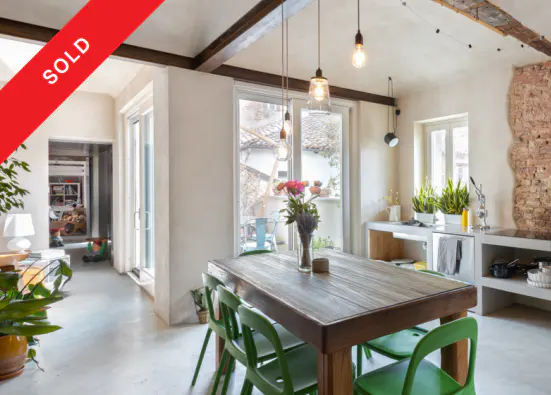 A bright, airy dining room with a wooden table, green chairs, and a vase of flowers. "SOLD" banner in the upper left corner.