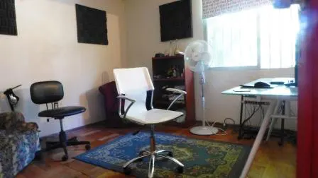 A home office with a white desk, white chair, black chair, fan, and blue rug.