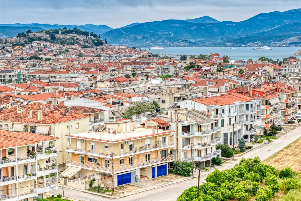 Cityscape view of Nafplio, Greece, with red-tiled roofs, white buildings, and mountains in the background.