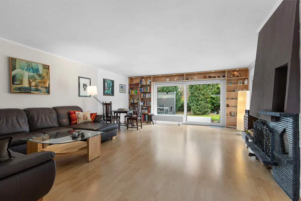 Living room with brown leather sofa, glass table, fireplace, and sliding glass doors to a green yard.