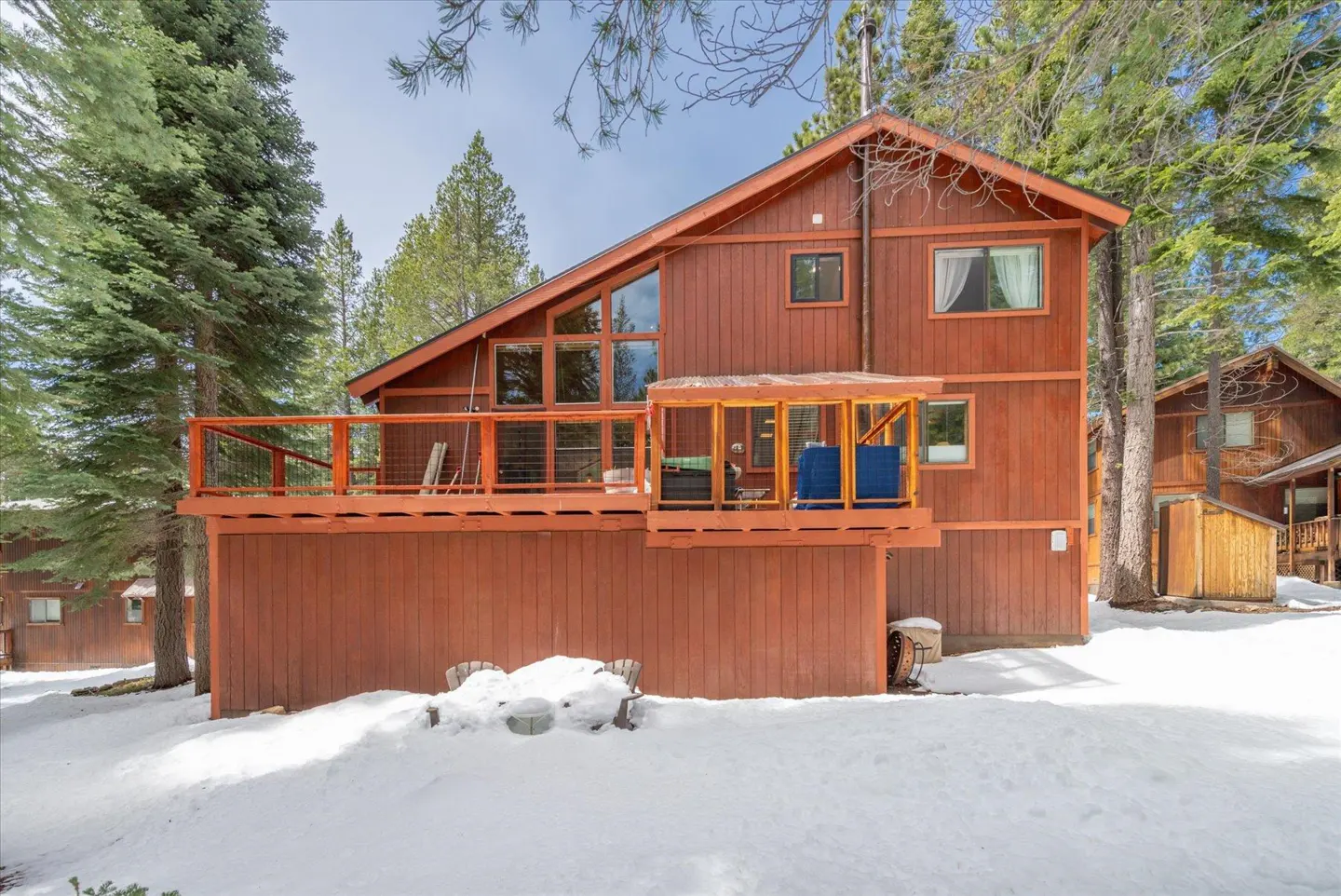Exterior view of a two-story brown house with a deck, surrounded by snow and trees.