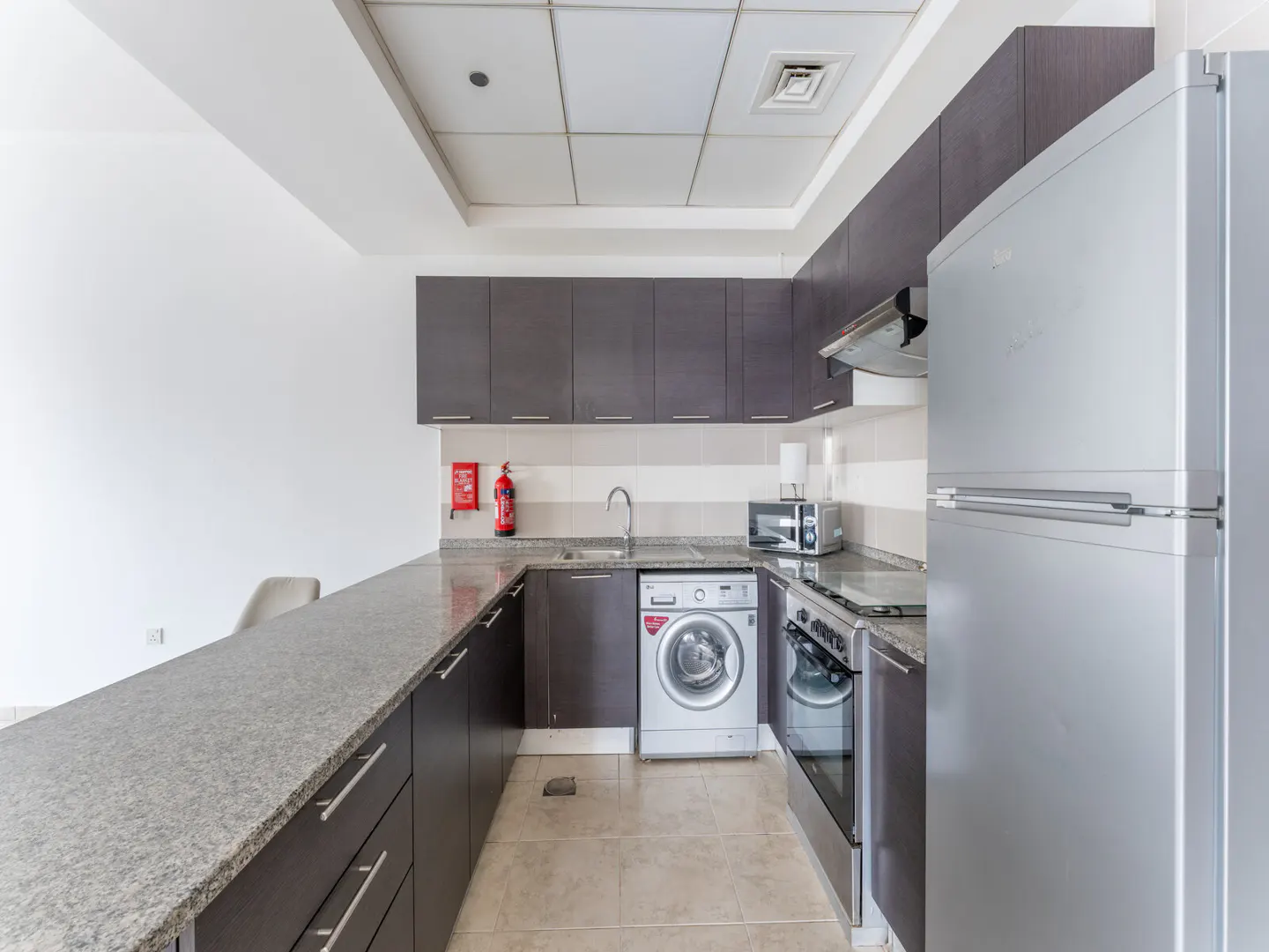 A modern kitchen with gray cabinets, granite countertops, and stainless steel appliances including a refrigerator, oven, and washing machine.