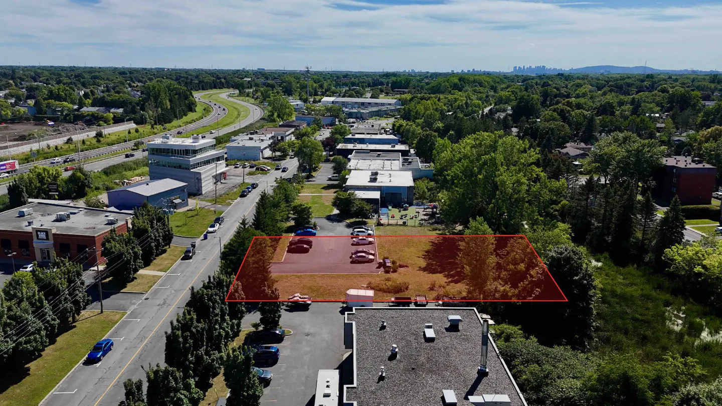 Aerial view of a rectangular lot outlined in red, with parked cars, surrounded by buildings and trees.