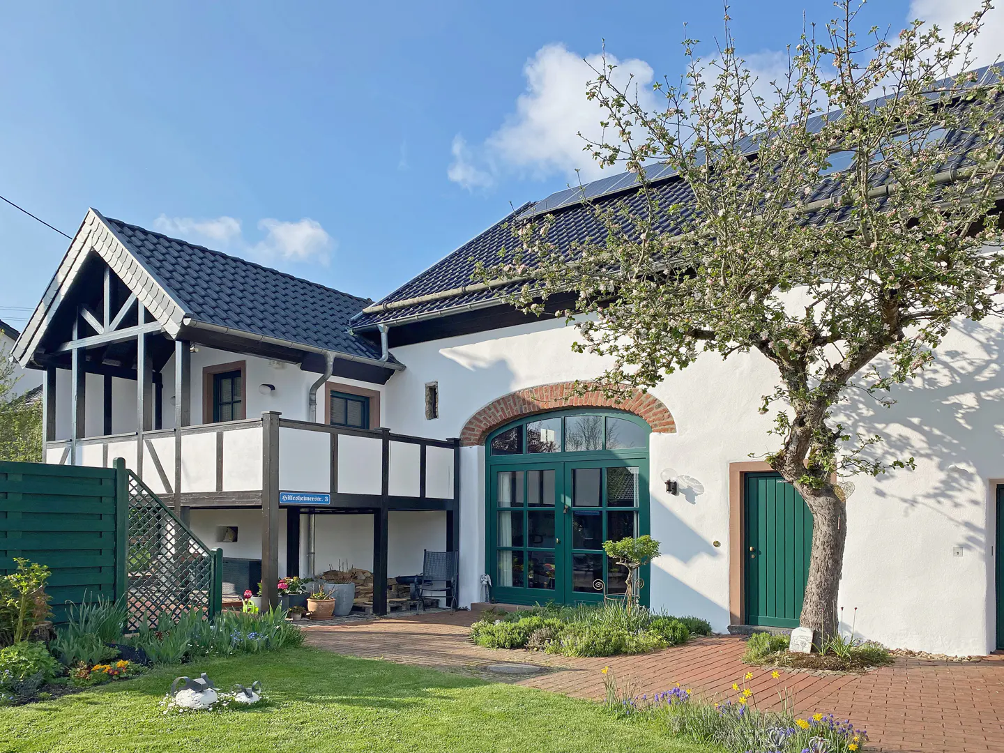 Two-story white house with dark roof, green trim, and blooming tree in the yard.