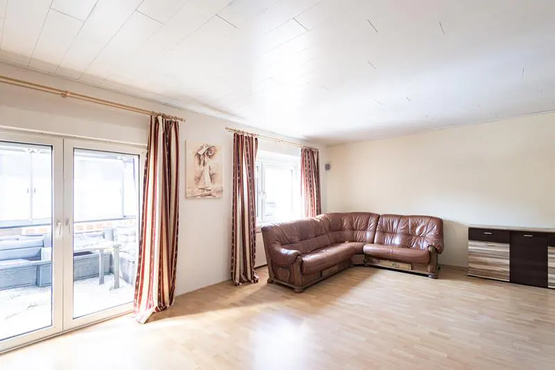 Bright living room with wood floors, brown leather sectional sofa, and sliding glass doors to a patio.