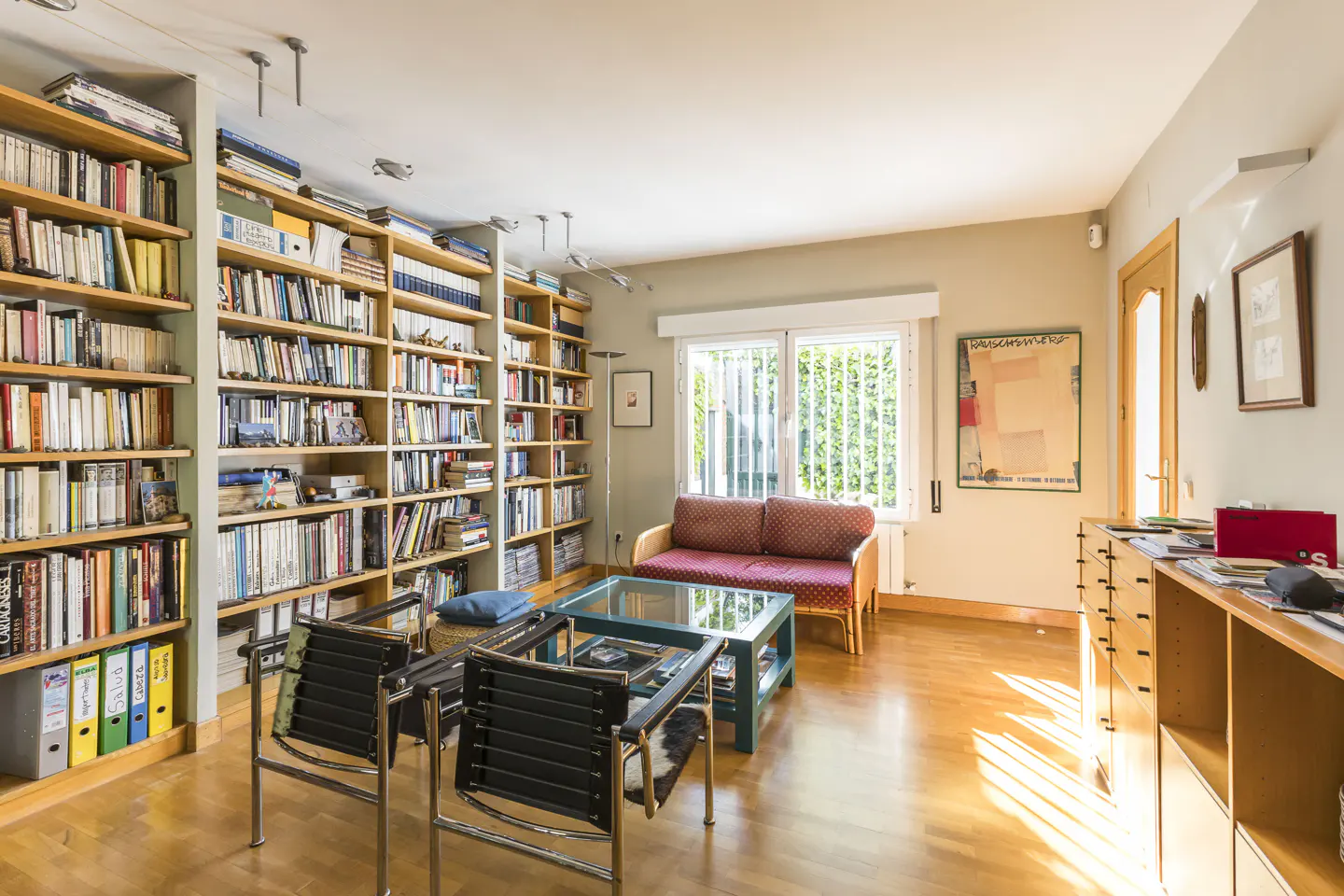 Bright living room with hardwood floors, floor-to-ceiling bookshelves, a red sofa, and two black chairs.