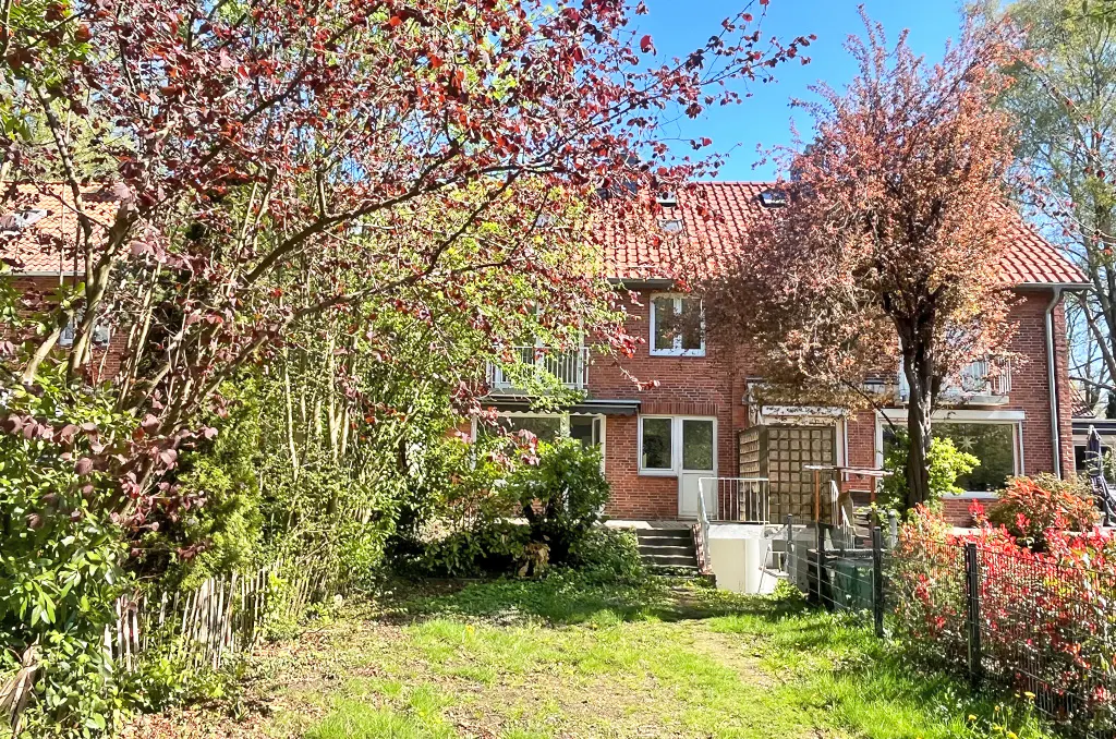 A two-story brick house with a red tile roof, viewed from the backyard with trees and green grass.
