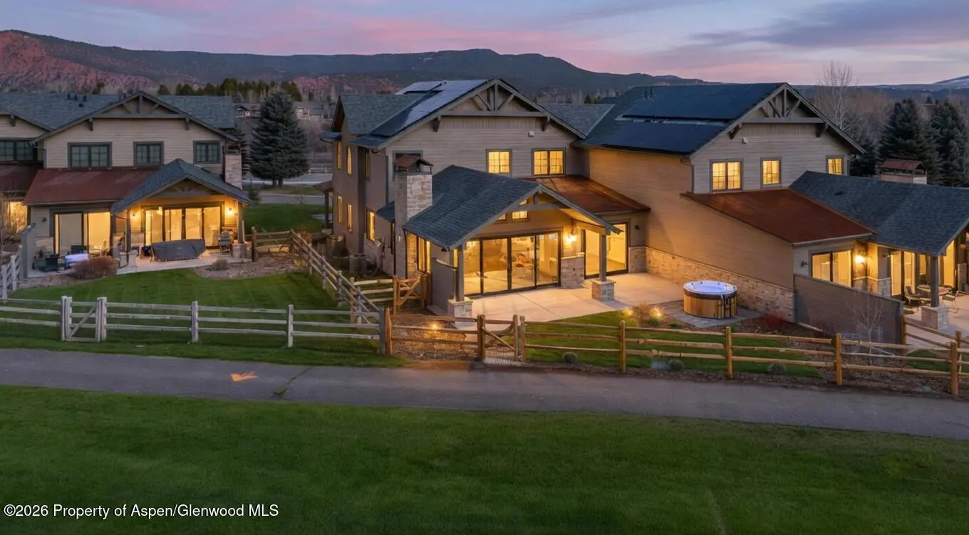 Exterior view of tan townhouses with solar panels, wooden fences, and mountain backdrop at dusk.