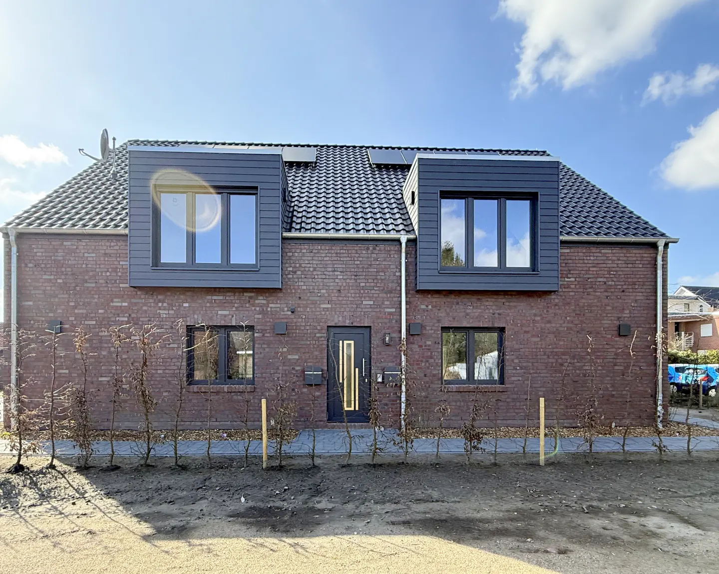 Two-story brick house with dark gray trim, windows, and door under a blue sky.