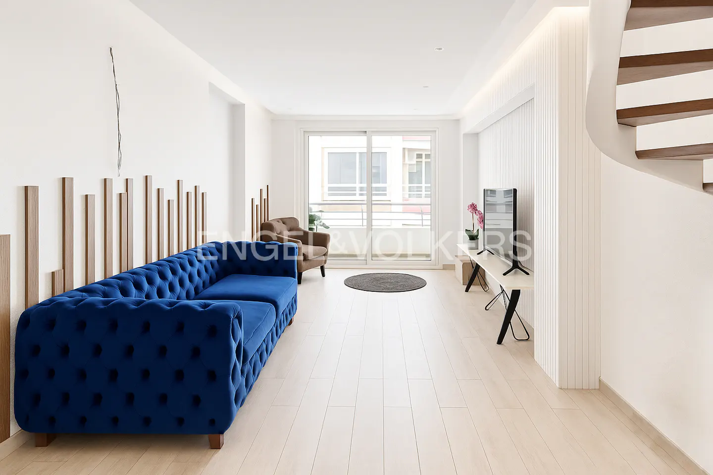 Bright living room with a blue tufted sofa, brown armchair, TV, and sliding glass doors to a balcony.