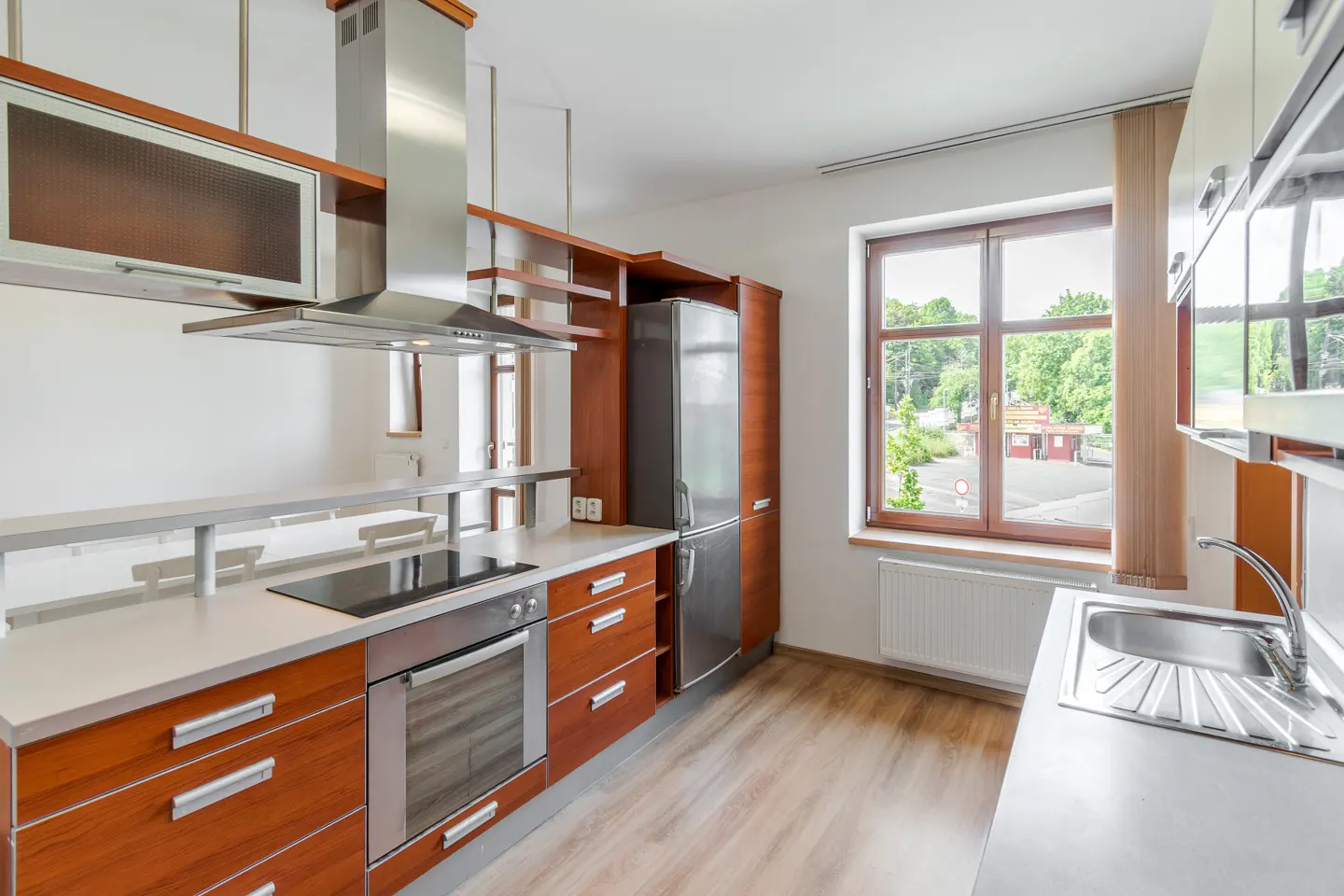 Modern kitchen with wood-tone cabinets, stainless steel appliances, a built-in oven, and a window overlooking greenery.
