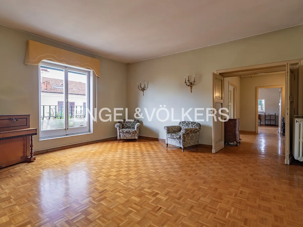 Spacious living room with parquet flooring, two patterned armchairs, and a large window with a yellow valance.