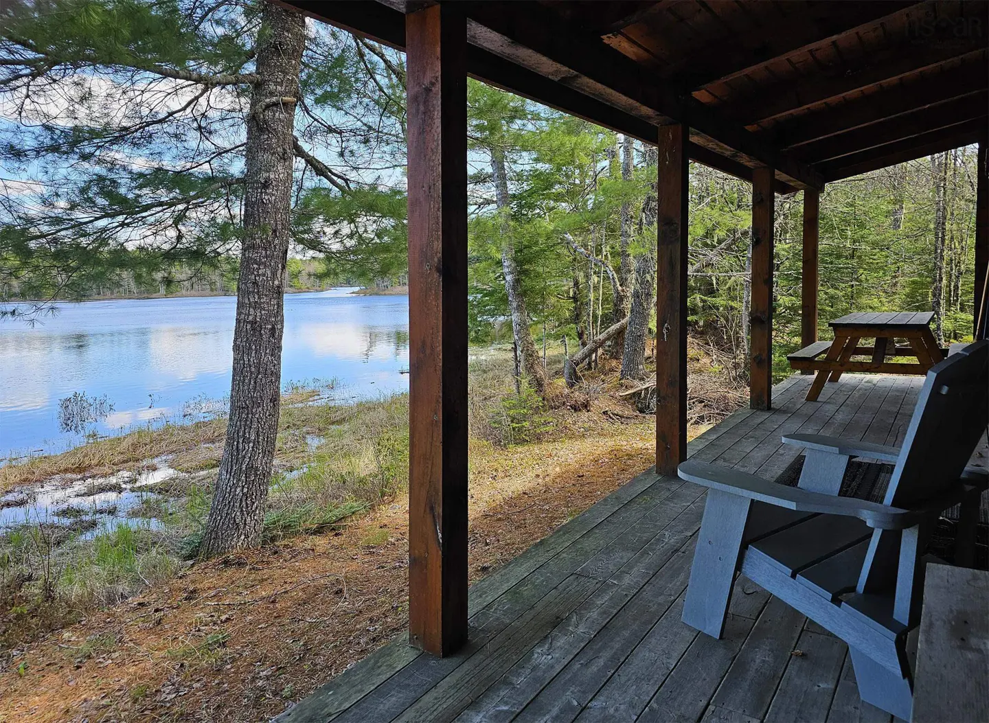 View from a cabin porch with blue chairs and a picnic table, overlooking a lake and trees.