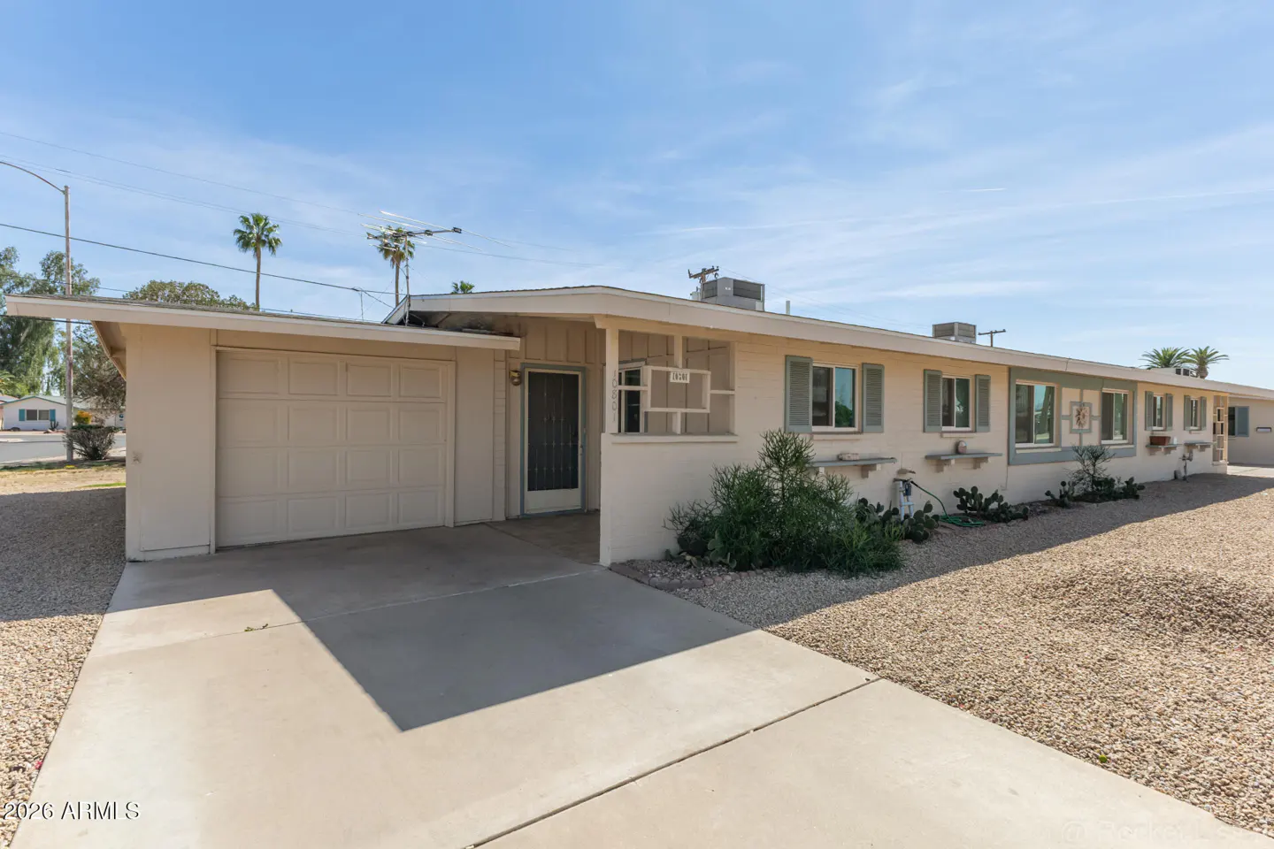 Beige single-story home with a garage, a dark front door, and green shutters under a blue sky.