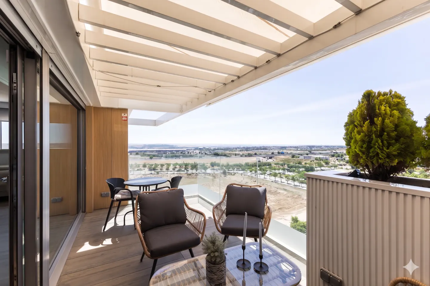 Modern balcony with a pergola, wicker chairs, a small table, and a scenic view of the landscape under a clear blue sky.