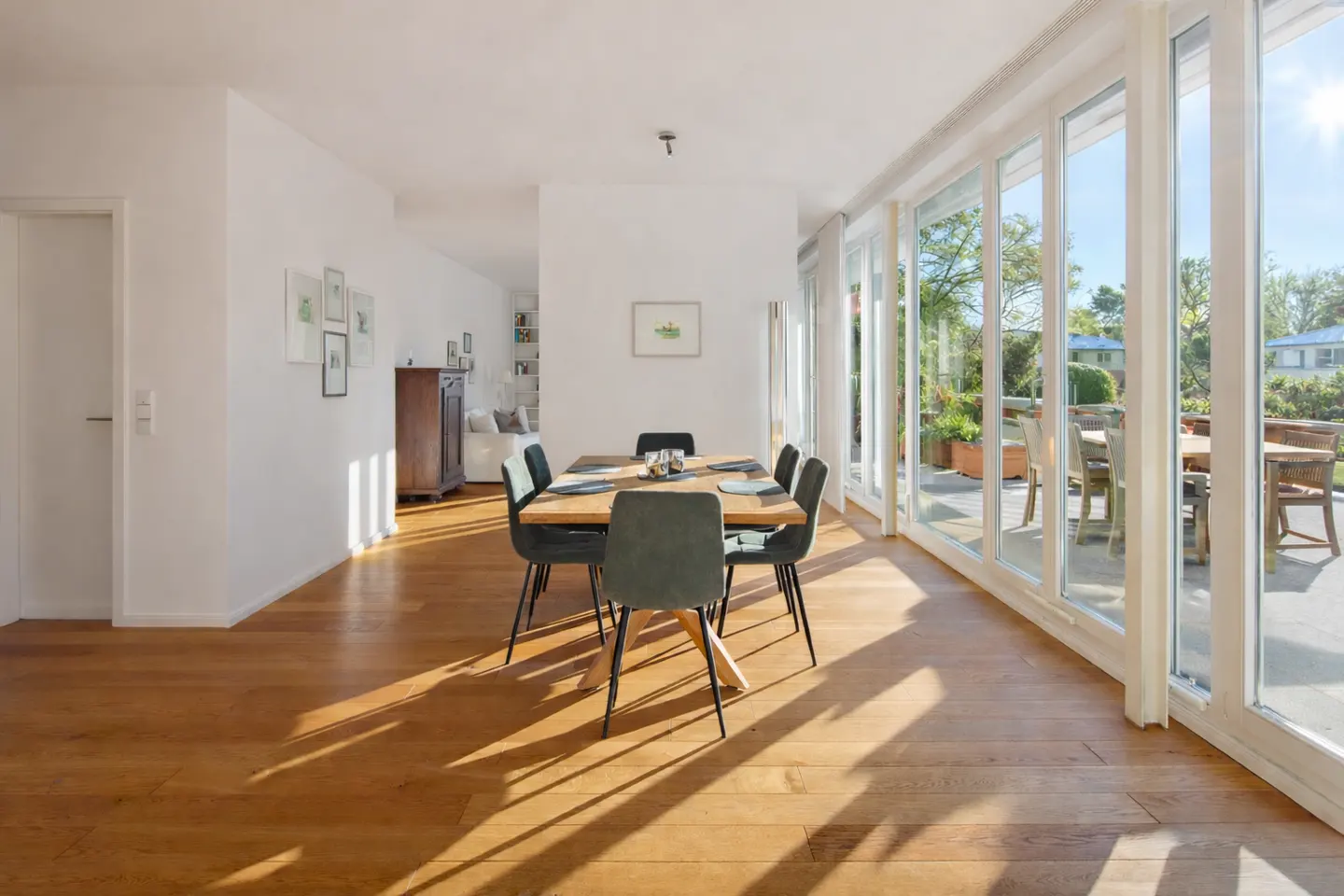 Bright dining room with wood floors, a table with six chairs, and large windows overlooking a patio.