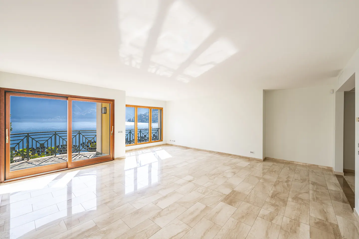 Bright, empty room with marble floors and white walls. Sliding glass doors open to a balcony with a view of the ocean.