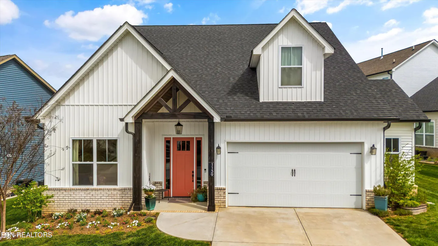 A white, two-story house with a gray roof and a salmon-colored front door. A white garage door is on the right.