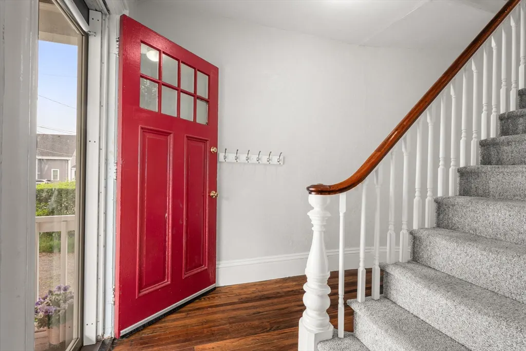 Entryway with an open red door, hardwood floors, and a carpeted staircase with a white banister.