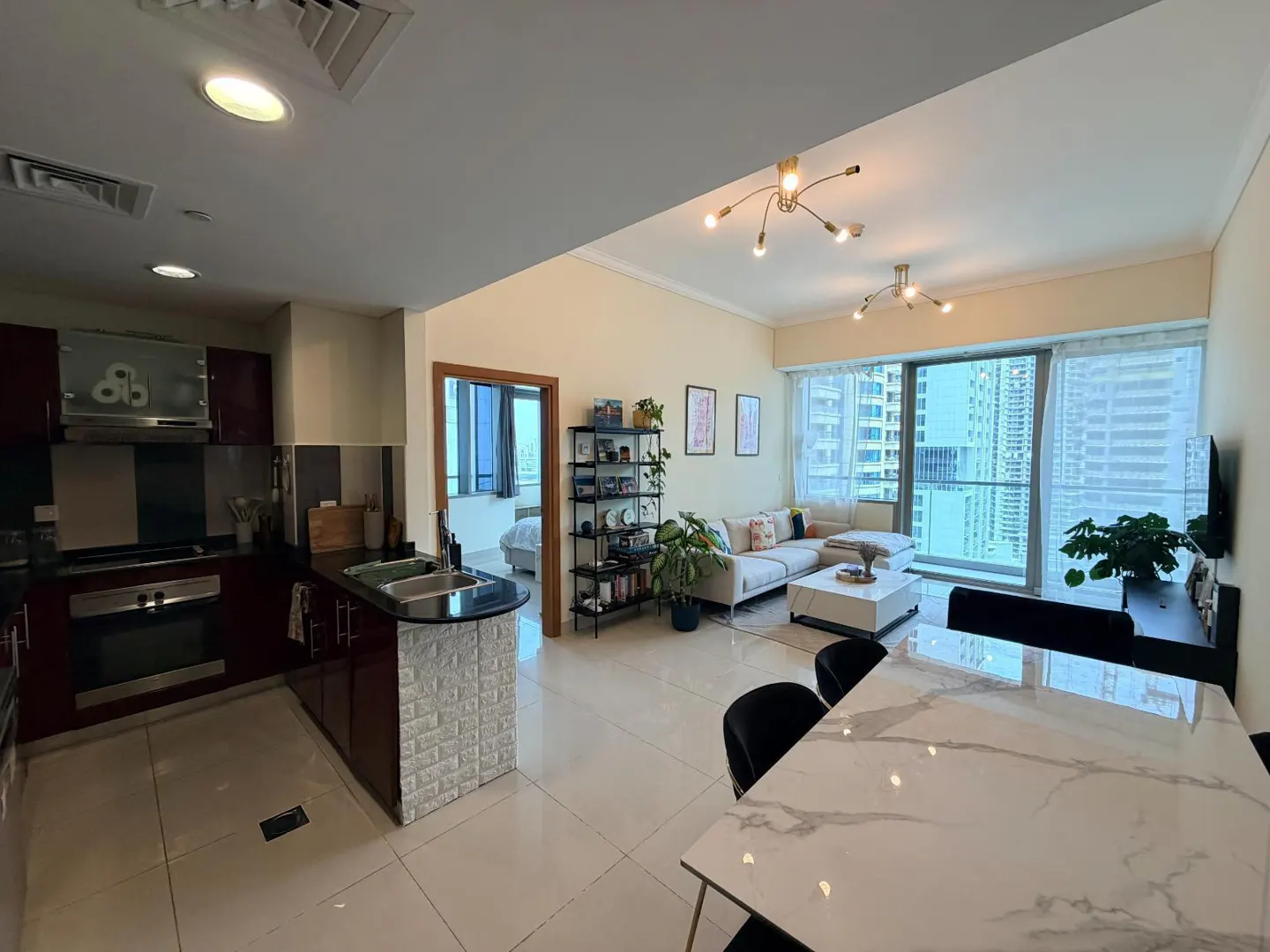Open-concept apartment with kitchen, dining, and living areas. Features include a marble table, sectional sofa, and city views.