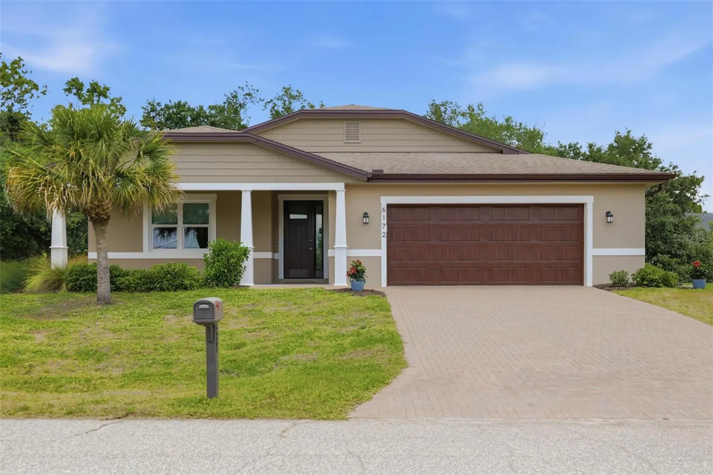 Beige single-story home with a brown roof and a two-car garage. A palm tree stands in the front yard.