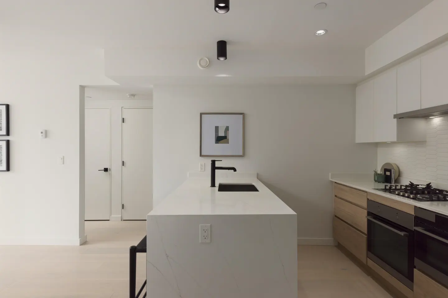 Bright, modern kitchen with white cabinets, a quartz island with a black faucet, and stainless steel appliances.