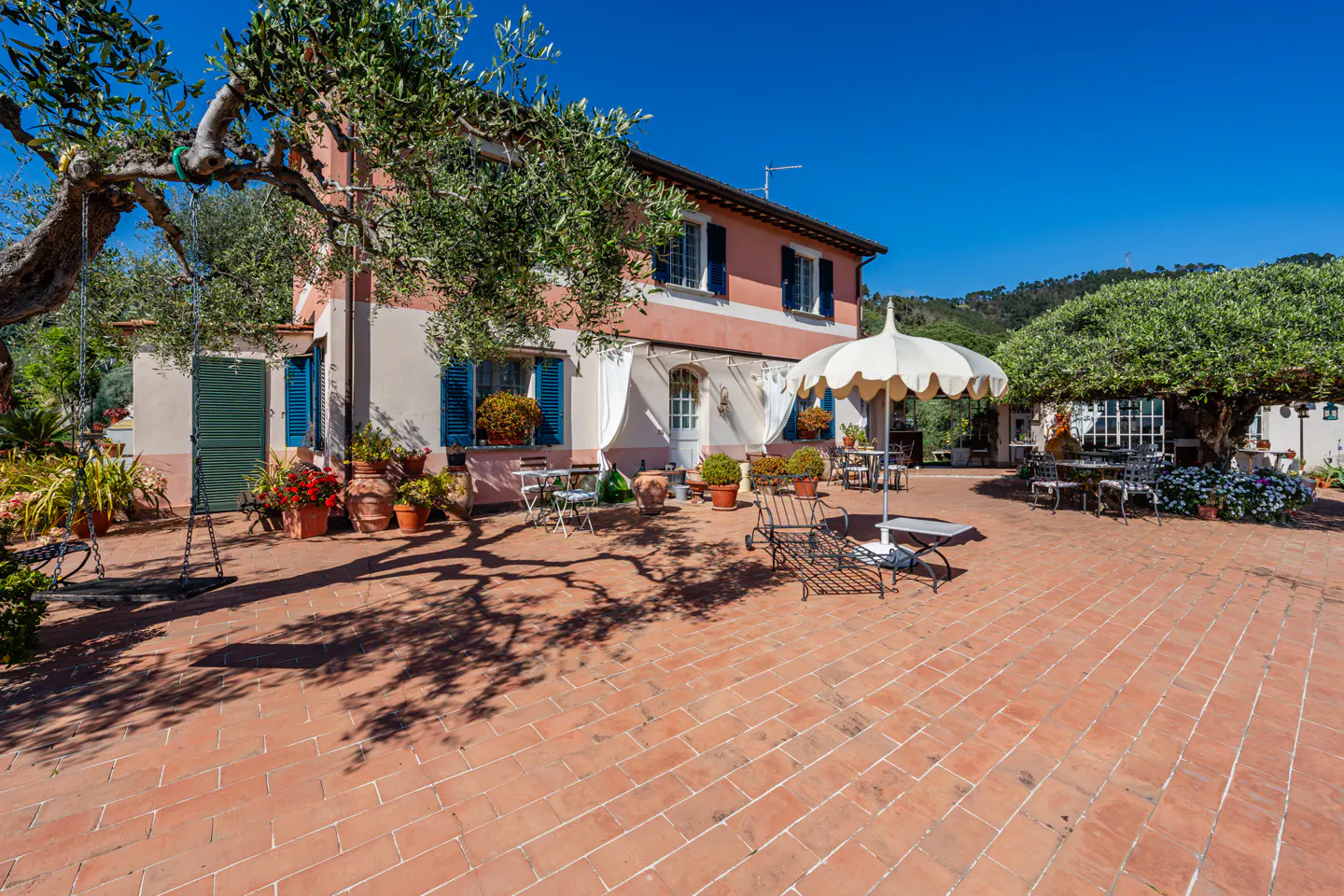 Exterior view of a two-story pink house with blue shutters and a red brick patio with outdoor furniture.