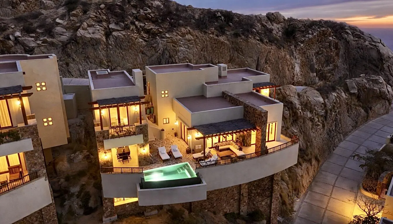 Luxury villa perched on a rocky cliffside with a pool, lounge area, and balconies overlooking the ocean at dusk.