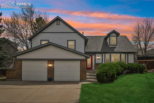 Two-story gray house with a red door, two-car garage, green lawn, and a colorful sunset sky.