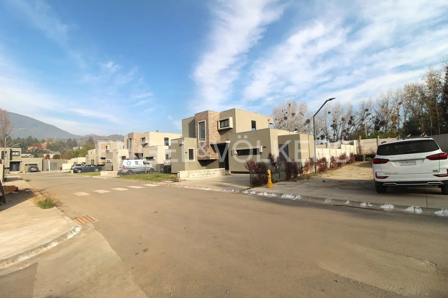 Street view of modern, two-story, beige homes with a white SUV parked in front. Blue sky with scattered clouds above.