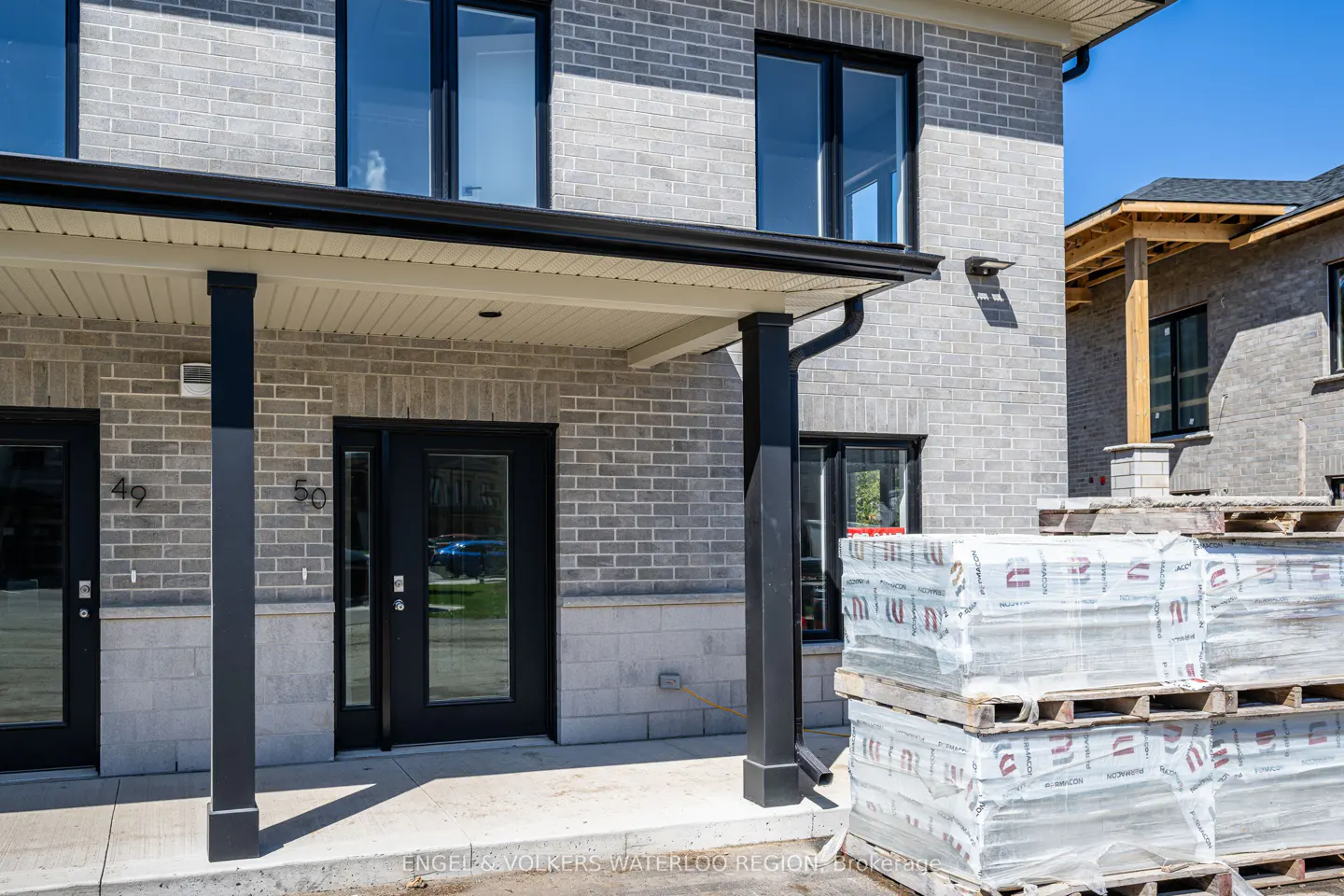 Exterior of a new gray brick townhouse with black door and window trim, and construction materials stacked in front.