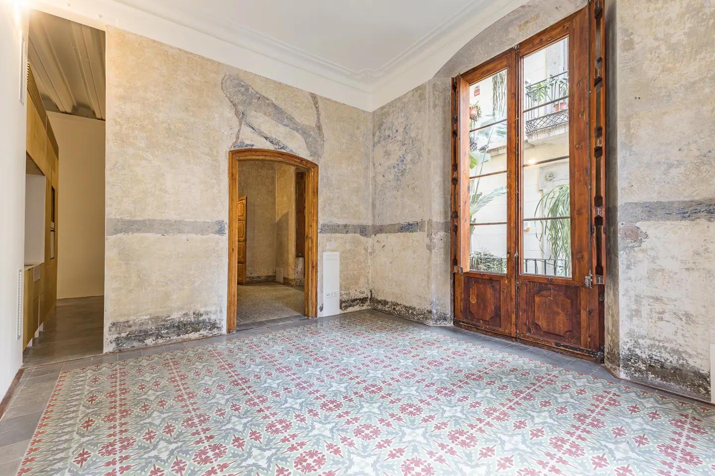 Empty room with patterned tile floor, textured walls, and open wood-framed doors to a balcony.