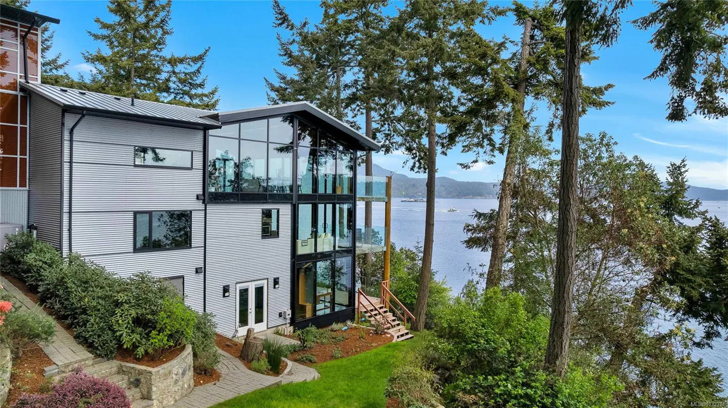 Modern three-story home with corrugated metal siding and large windows overlooking the ocean. Trees surround the property.