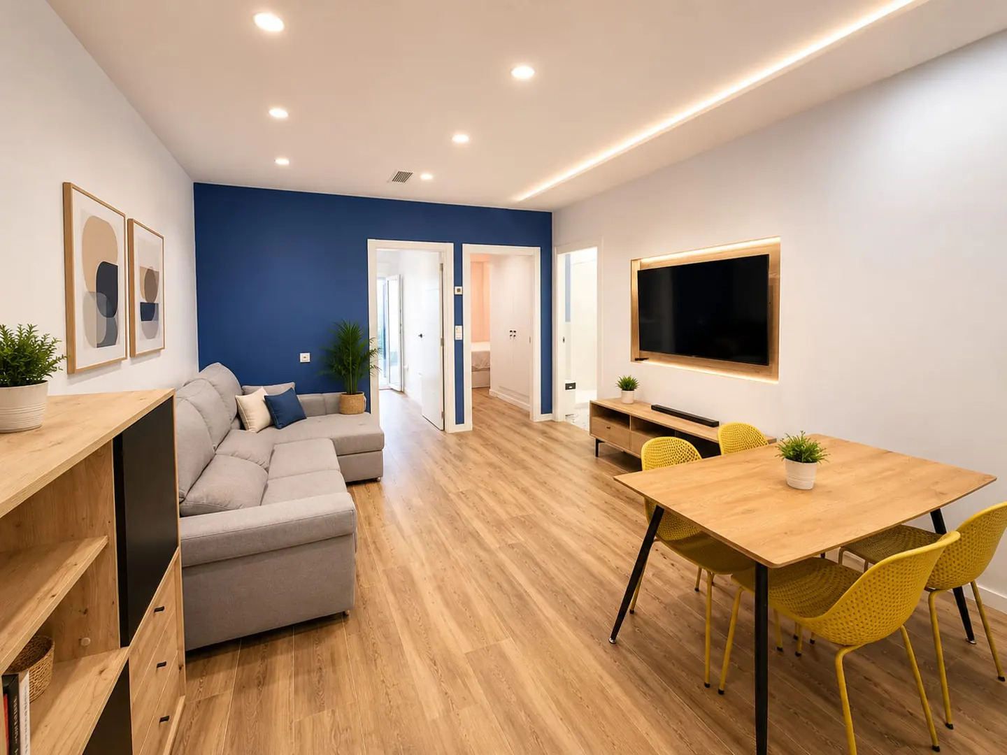 Bright, modern living room with gray sectional sofa, blue accent wall, wood floors, and a dining table with yellow chairs.