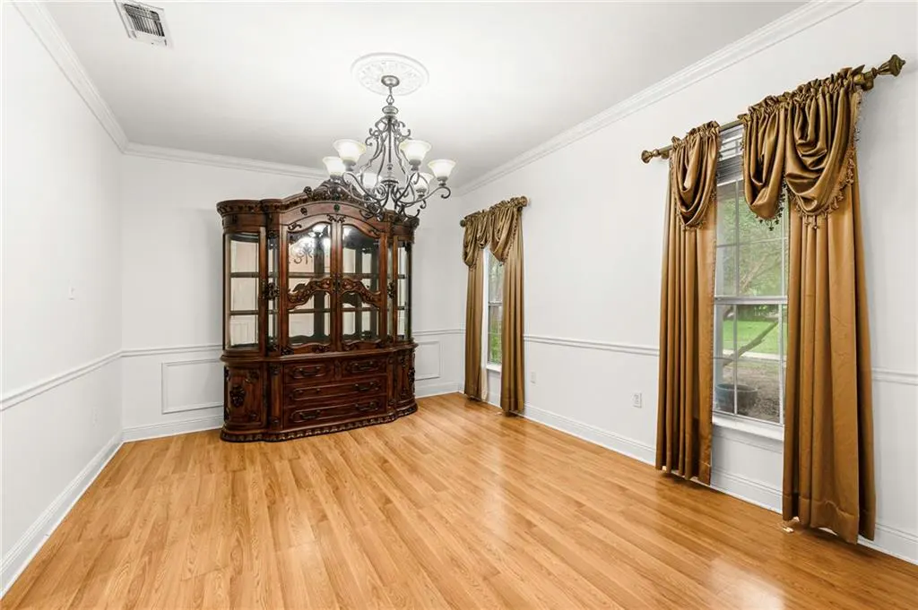A dining room with hardwood floors, white walls, and gold curtains. A dark wood china cabinet and chandelier add elegance.