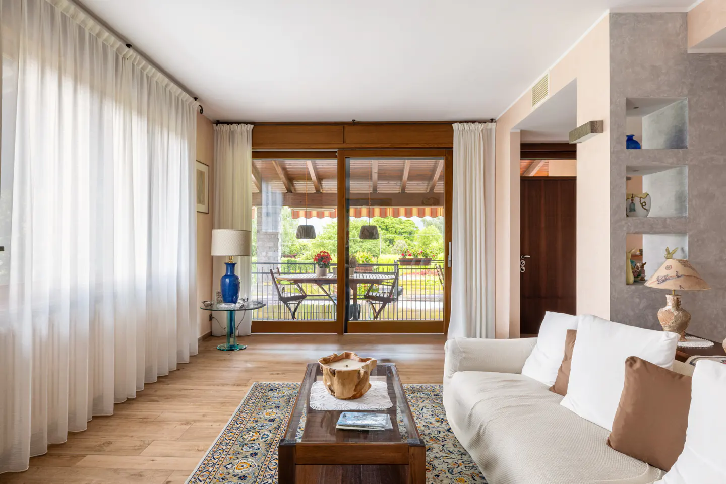 Bright living room with white sofa, wooden coffee table, blue lamp, and sliding glass doors leading to a patio.