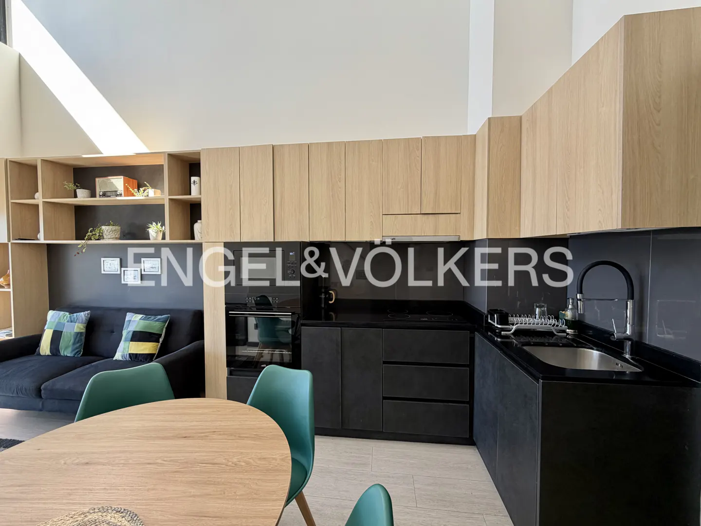 Open-concept living space with a black sofa, green chairs, and a modern black and wood kitchen.