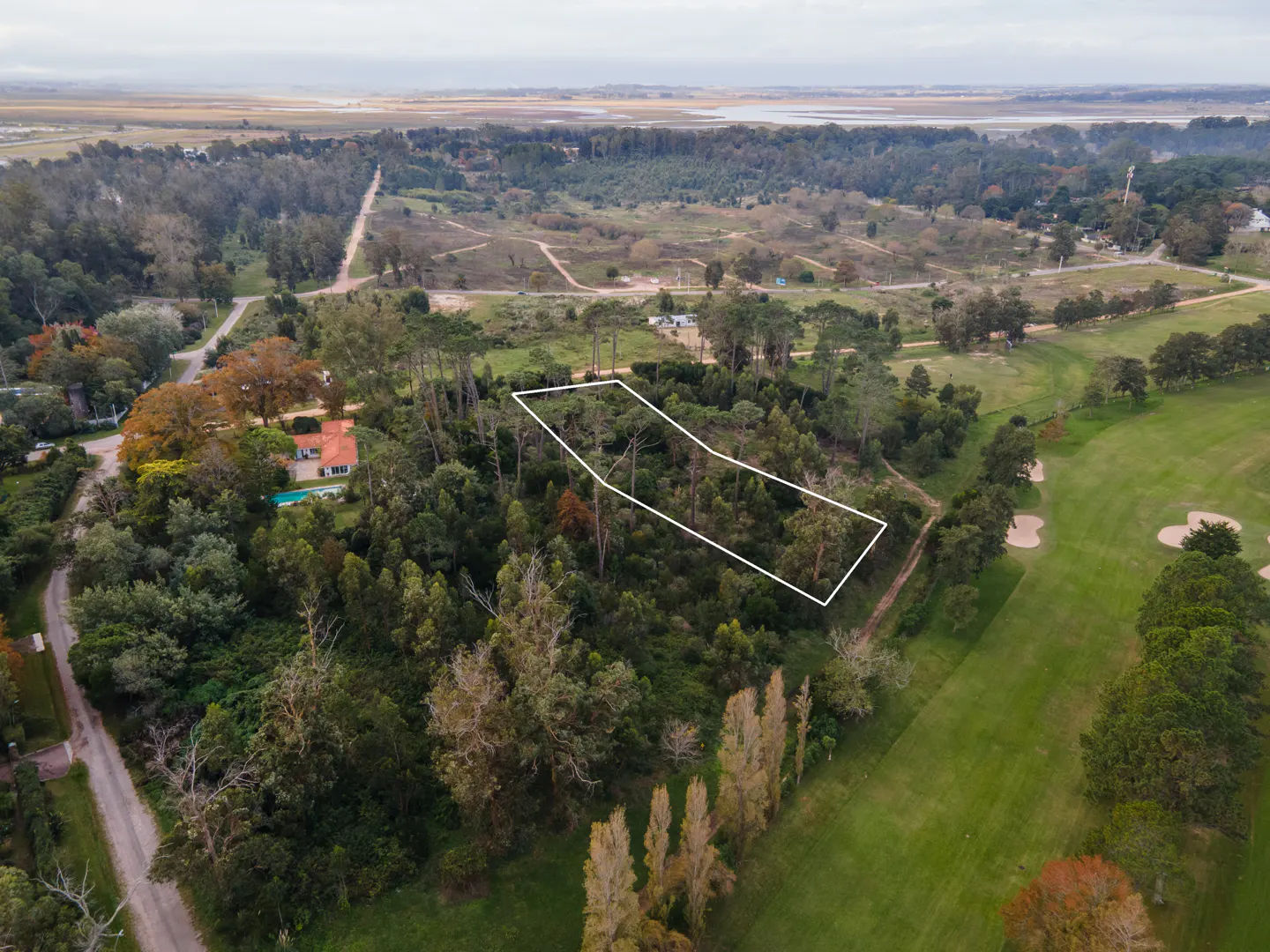 Aerial view of a wooded lot outlined in white, adjacent to a golf course and near a body of water.