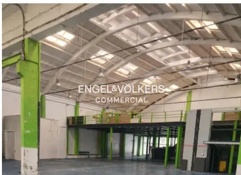 Large commercial space with high ceilings, skylights, and a mezzanine level. Green support beams and Engel & Völkers Commercial logo.