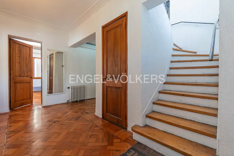 Hallway with wood floors, white walls, and wooden doors. A staircase with white risers and wooden treads is on the right.