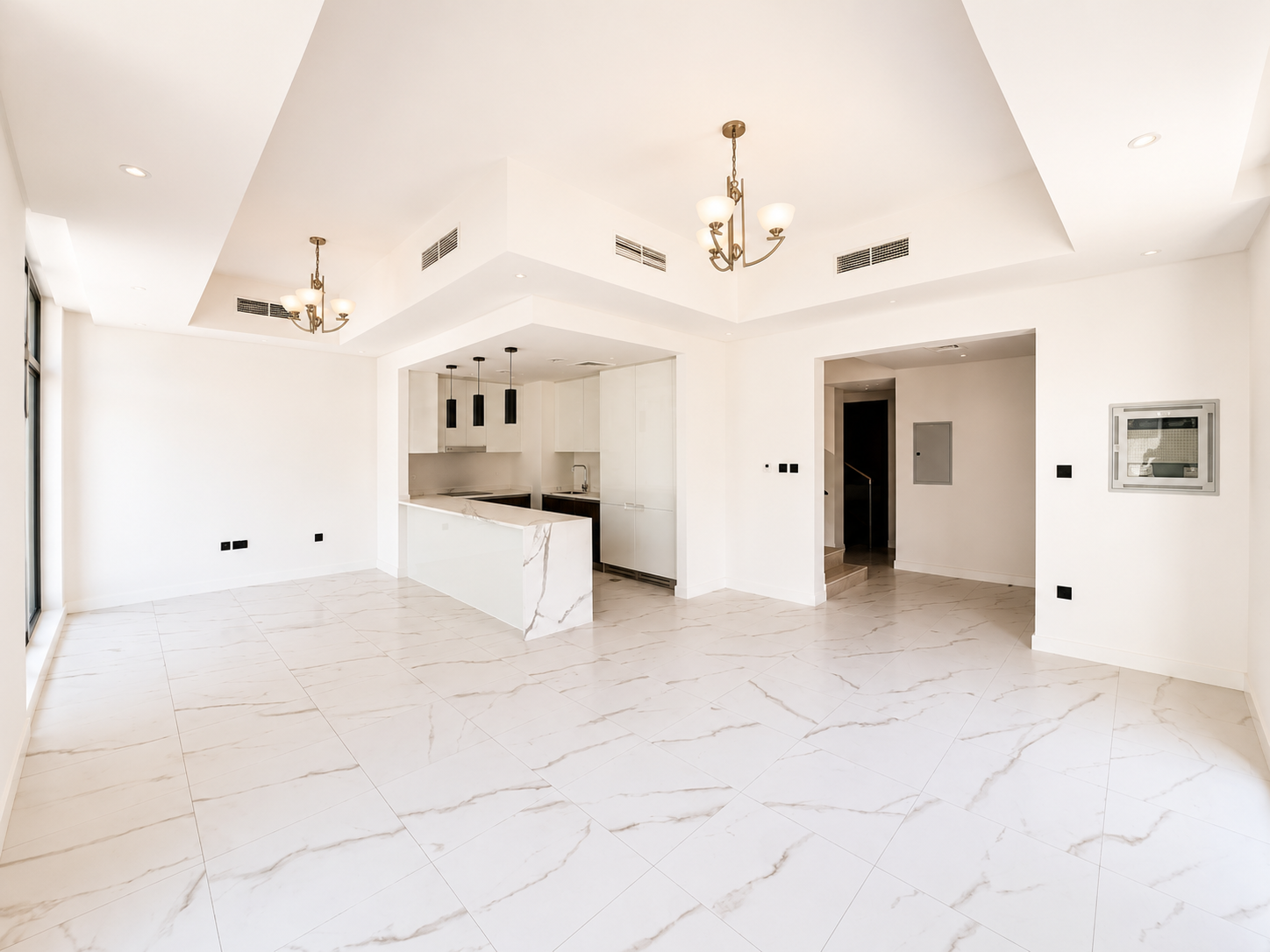 Modern open-plan living area with white marble floors, a kitchen island, and elegant chandeliers in a bright, white room.