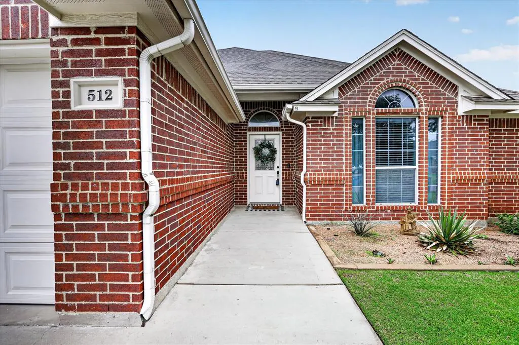 Exterior of a red brick house with a white front door and a concrete walkway. The house number "512" is visible on the brick wall.
