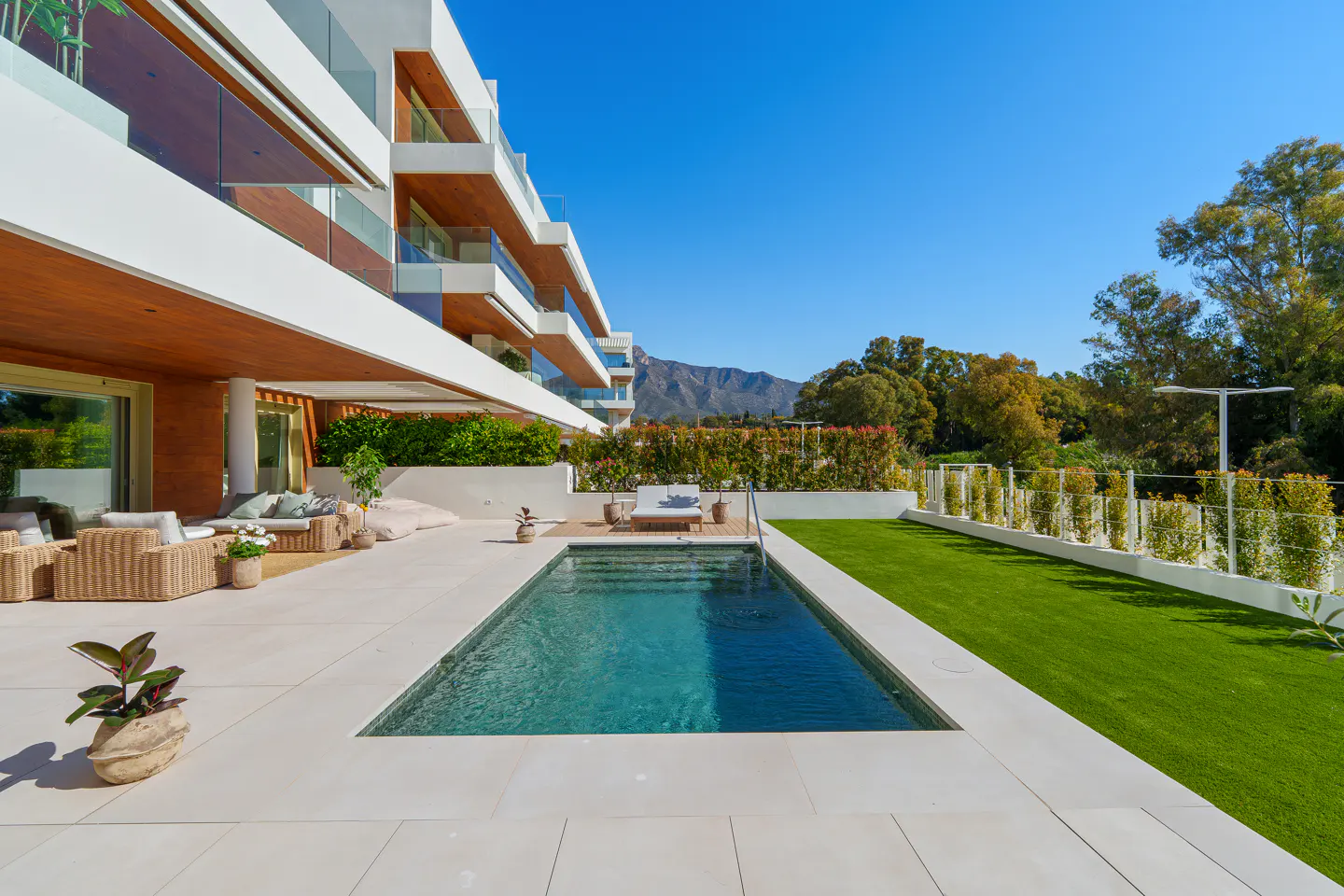 Modern white building with a pool, patio furniture, and green lawn under a clear blue sky.