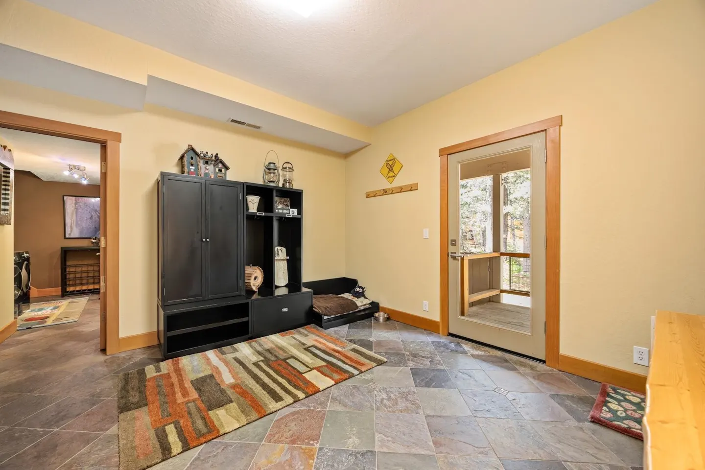 Entryway with slate tile floors, a black storage unit, a pet bed, and a glass door leading to a wooden deck.