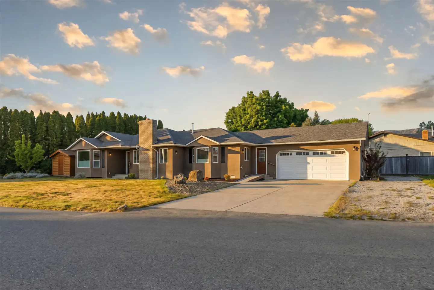 A single-story brown house with a white garage door and a gray roof under a cloudy sky.