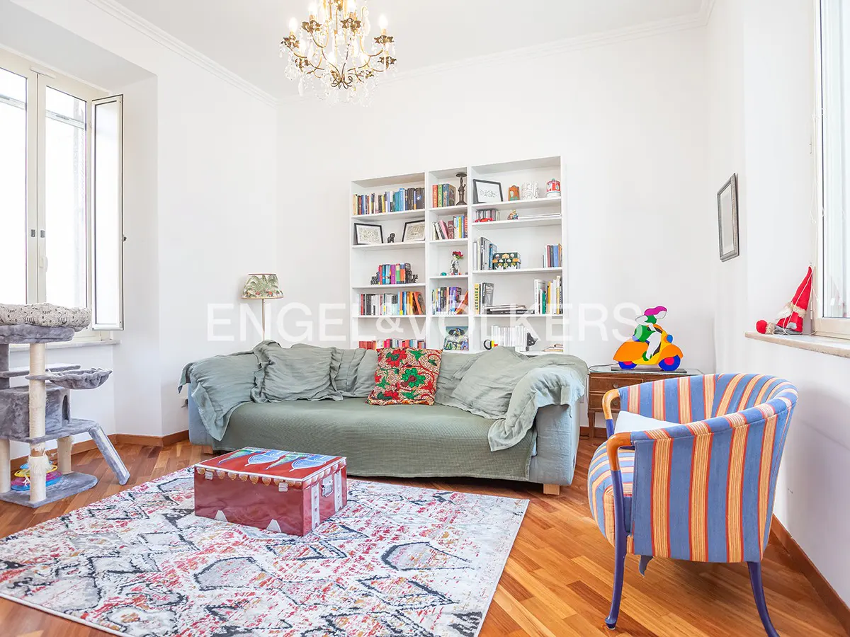 Bright living room with a green sofa, colorful rug, and a blue and orange striped chair. A white bookcase is in the background.