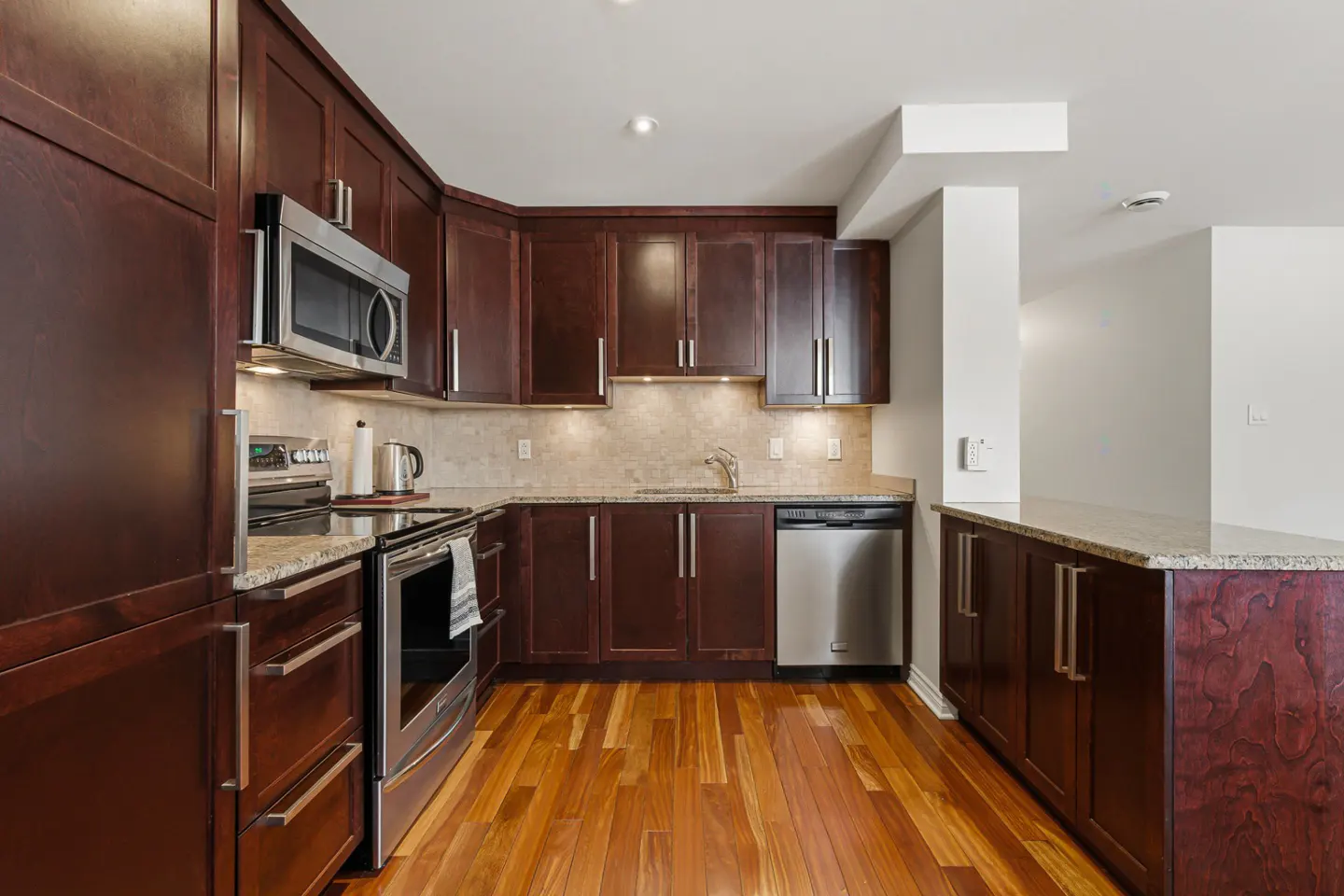 A modern kitchen with dark wood cabinets, stainless steel appliances, granite countertops, and hardwood floors.