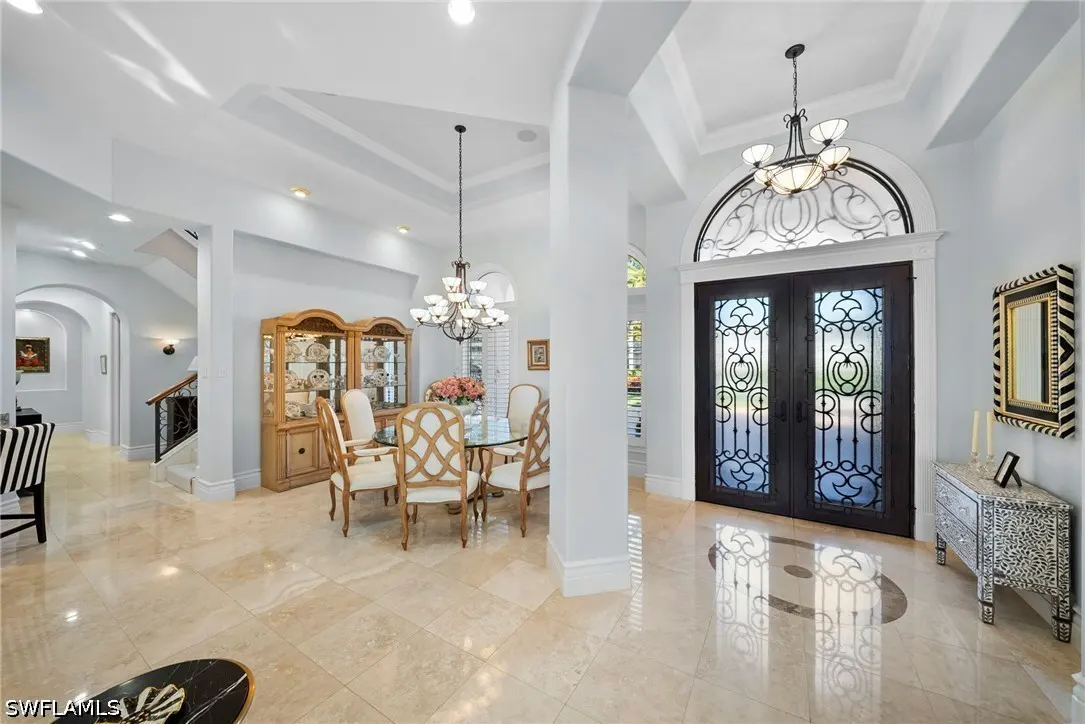 Bright foyer with marble floors, a dining table, and a dark wood door with an arched window above.