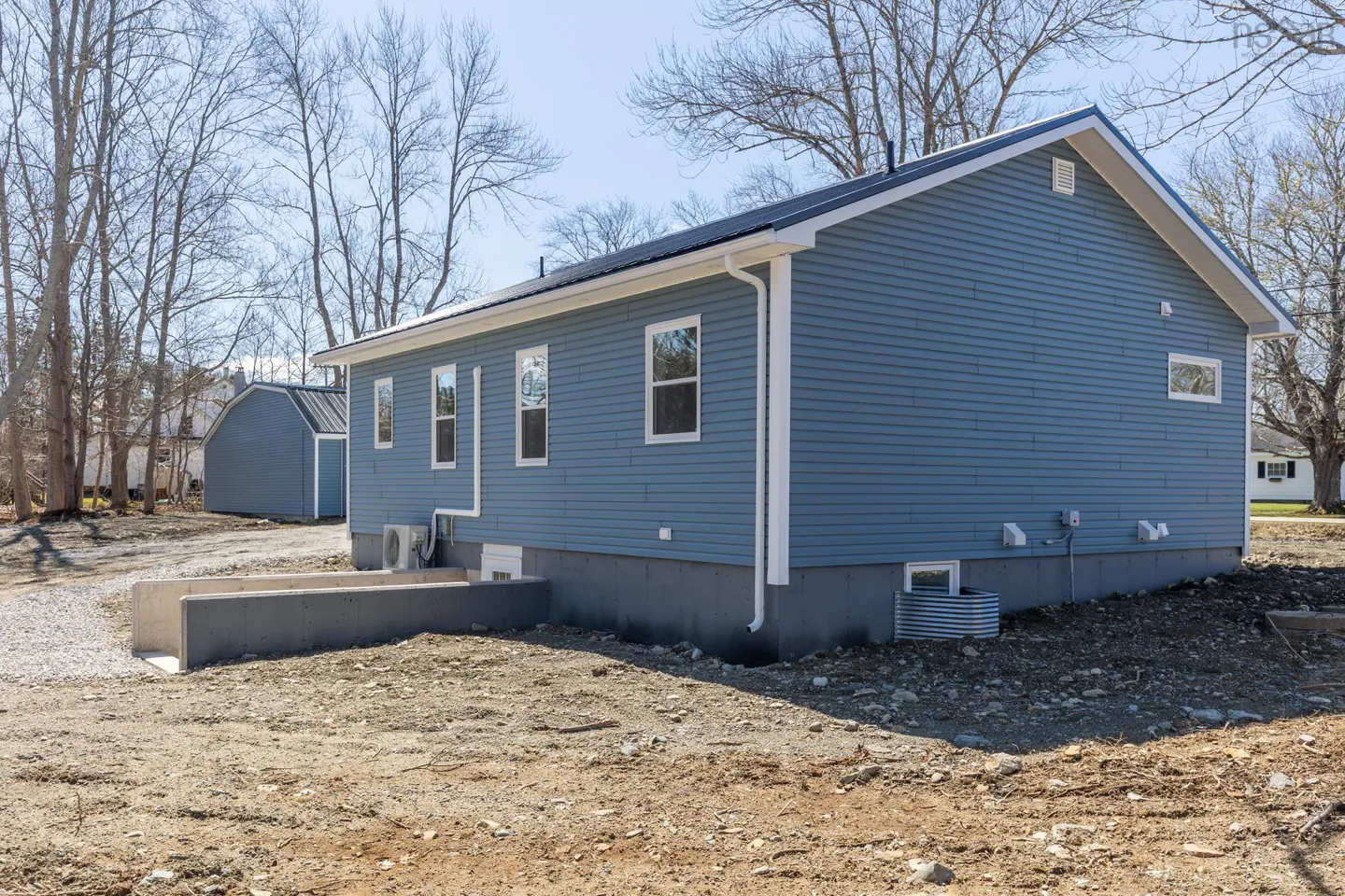 Side view of a blue house with white trim, a gray foundation, and a black roof. A shed is visible in the background.